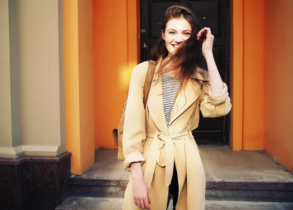 Jovem elegante menina hipster vestindo casaco de trincheira moderna andando na cidade urbana sorrindo feliz . — Fotografia de Stock