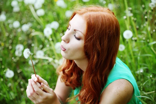 Retrato de estilo de vida de una joven mujer de moda de primavera que sopla diente de león en el jardín de primavera . — Foto de Stock