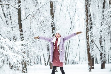 Kış karlı parkta elleri açık genç bir kadın.