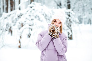 Kışın karlı parkta eldiven takan genç bir kadın.