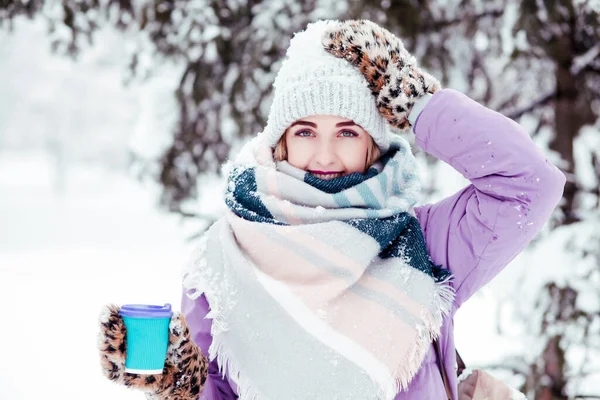 young woman holding coffee  in winter snowy park