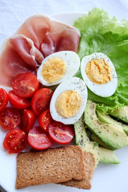 Haşlanmış yumurta, pastırma, avokado, tost, domates ve salata.