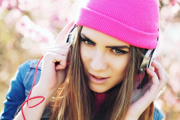 Close up portrait of a funny young swag girl on lush garden listening to music in earphones from smart phone mp3 player.