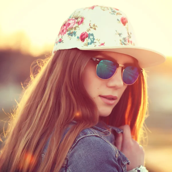Szabadtéri divat elegáns szajré lány, rajta sapka szajré, divatos napszemüveg és farmer dzseki, csodálatos kilátás nyílik a tengerparton napnyugtakor portréja. — Stock Fotó