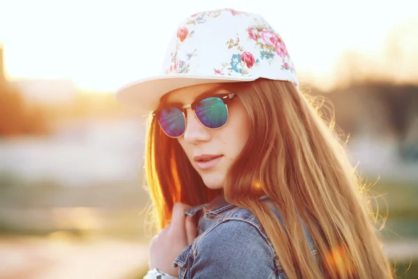 Açık moda yağma kap, trendy güneş gözlüğü ve denim ceket, şaşırtıcı günbatımı vasıl belgili tanımlık kıyı görünümünü giyen şık yağma kız portresi.