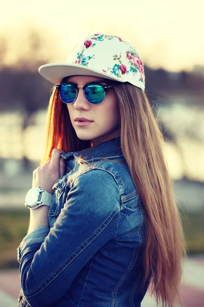 Açık moda yağma kap, trendy güneş gözlüğü ve denim ceket, şaşırtıcı günbatımı vasıl belgili tanımlık kıyı görünümünü giyen şık yağma kız portresi.