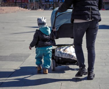 Çocuğu olan bir kadın ve kaldırımda bir bebek arabası..