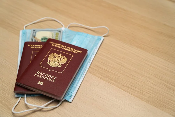 Passport with banknotes of 100 dollars and a medical mask on a wooden table. The concept of safe travel during epidemics