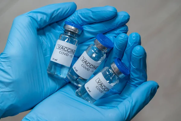 Close-up - hands of a doctor in protective sterile blue gloves holding a vaccine against coronavirus in the palms. Vaccination is a way to fight a pandemic and protect yourself from the virus.