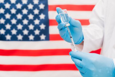 Aşı şişesi ve ABD bayraklı şırınga tutan doktor..