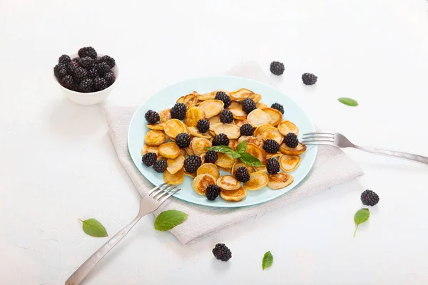 带有黑莓的迷你煎饼放在一个蓝色的盘子里 旁边有两个叉子 背景是白色的 — 图库照片