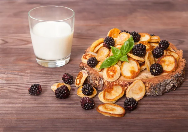 有黑莓和薄荷叶的小薄饼和放在木制桌子上的一杯牛奶 — 图库照片