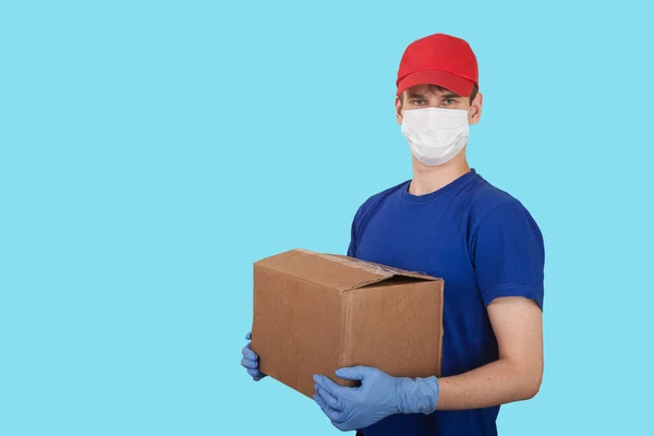 医療用マスクとゴム手袋の男性ボランティアは青い背景に箱を持っています 社会的援助 宅配便による商品の配送 — ストック写真