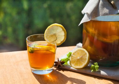 Cam bir kavanozda fermente edilmiş kombu çayı ve yeşil bir bahçenin arka planındaki ahşap bir masada limon standı ve içki bardağı..