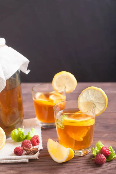 Kombucha in a glass jar, a glass with a drink and lemon slices on a wooden table on a black background. Fermented drink. Healthy food concept. Vertical — Stock Photo, Image