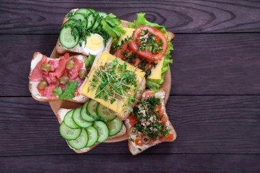 Kızarmış ekmek, krem peynirli sandviç, salatalık, domates, somon, lahanalar, kahverengi ahşap arka planda yumurta. Sağlıklı gıda konsepti. Düz yatıyordu. Boşluğu kopyala