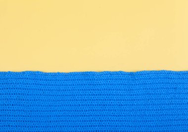 Elle örülmüş mavi bir eşarp parçası sarı bir arka planda yatıyor. El yapımı konsept