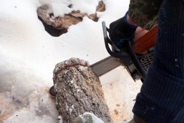 Bir adam kışın karda elektrikli testereyle odun kesiyor. Açık hava kavramı