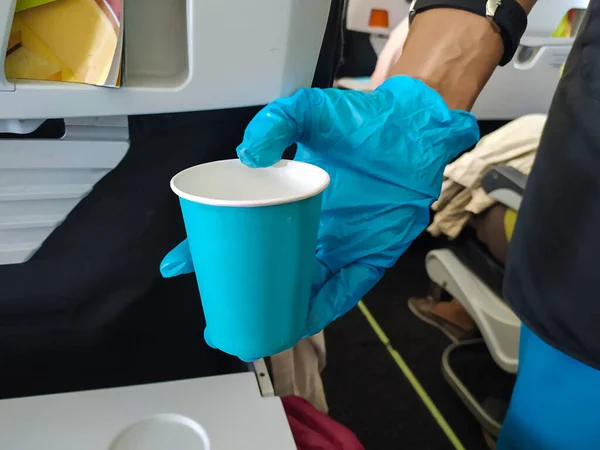 A flight attendant\'s hand in a blue rubber medical glove serves a paper cup with water. Security concept. Mobile Photo.