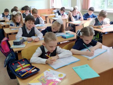 Öğrenciler, okul çocukları, kızlar ve oğlanlar sınıftaki masalarında ders çalışıyorlar. 22.04.2021