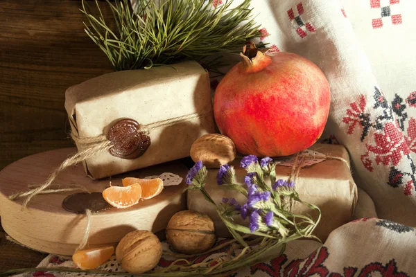 Pomegranate, walnuts and Christmas gifts among the flowers — Stock Photo, Image