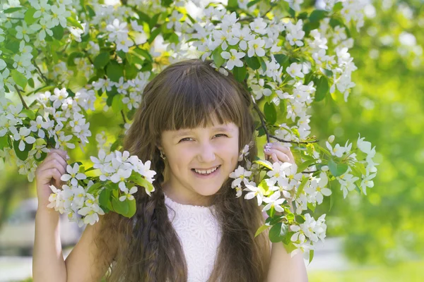 Leende flicka i grenarna på en blommande äppelträd — Stockfoto