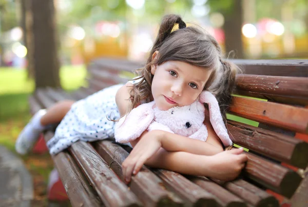 La chica está acostada en el banco con el conejo de juguete — Foto de Stock
