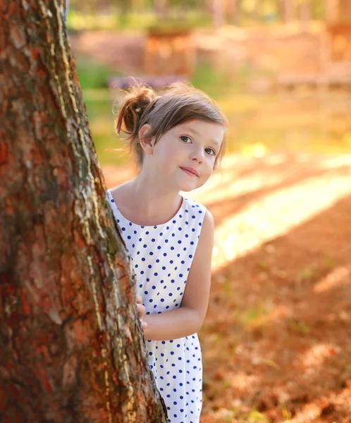 A girl looks out from behind a tree — Stock Photo, Image