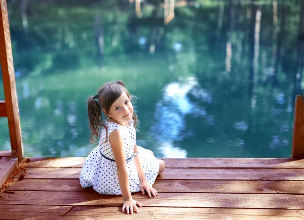 Smiling girl turned around sitting on the bridge by the pond — 스톡 사진