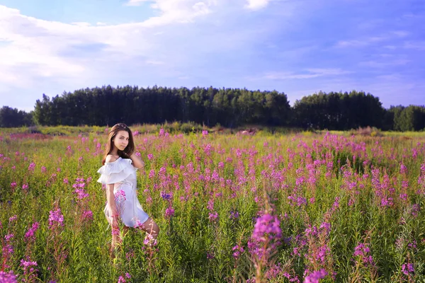 Uma jovem está em um campo de flores . — Fotografia de Stock