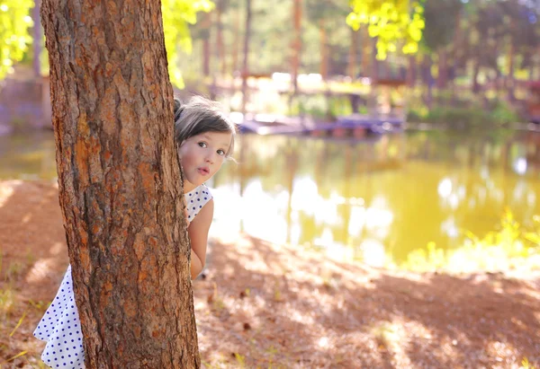 Flickan i parken vid dammen gömmer sig bakom ett träd — Stockfoto