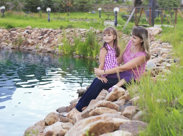 Mother with daughter sitting on the Bank of the pond — Stock Photo, Image