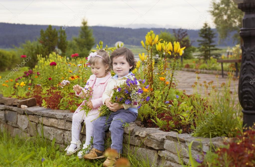 Boy and girl sitting in a flower bed with flowers