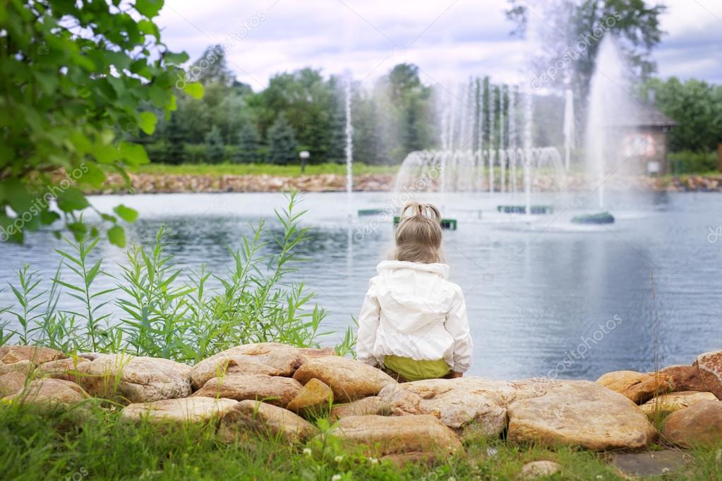 The little girl looks at the fountain at the pond