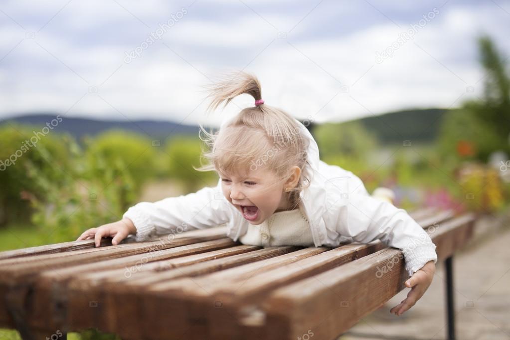 A little girl with delight lies on the bench