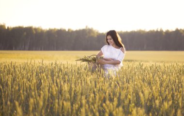 Beautiful girl in wheat field holding the basket with ears