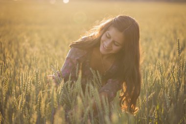 Smiling beautiful girl in a field looking at wheat grass