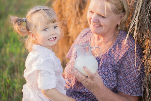 Grandma treats her granddaughter milk in a haystack — Stock fotografie