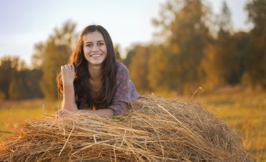 A smiling girl in a field lying on a haystack