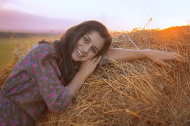 A beautiful girl was leaning against the haystack in the field