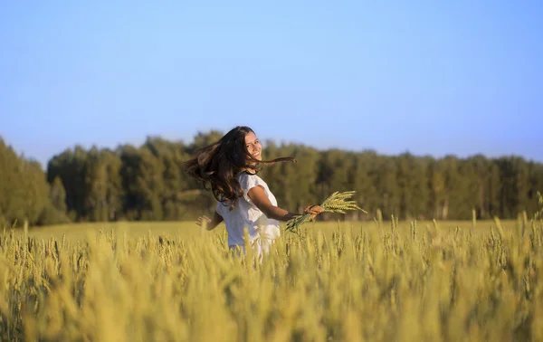 Chica sonriente en movimiento en un campo con espigas de trigo — Foto de Stock