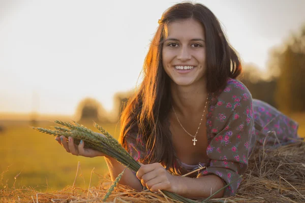 Morena sonriente al atardecer con espigas de trigo — Foto de Stock