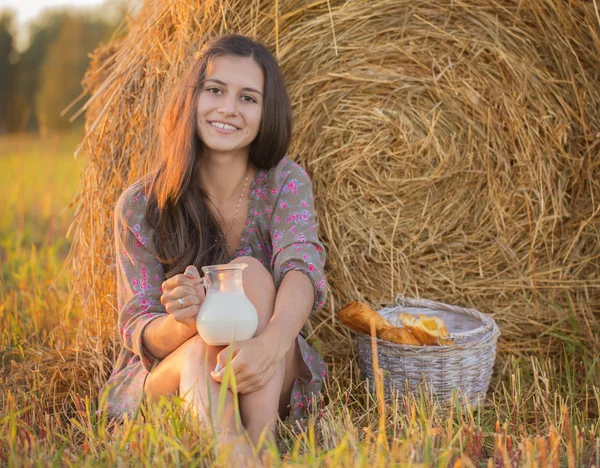 Smiling girl sits in a haystack at sunset — 图库照片