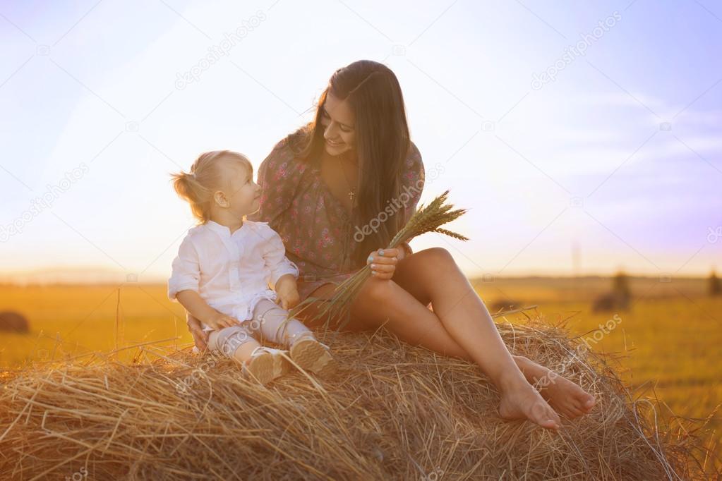 A young woman with a baby in the hay in the field