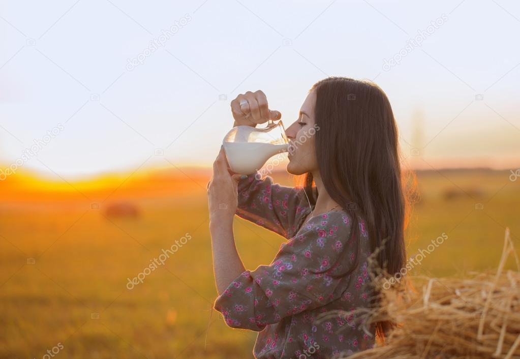 Young woman drinking milk from the jug at sunset