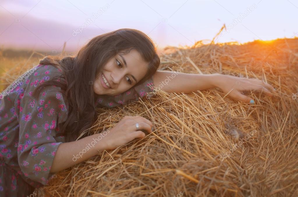 Smiling girl leaned on hay and looking at the straw