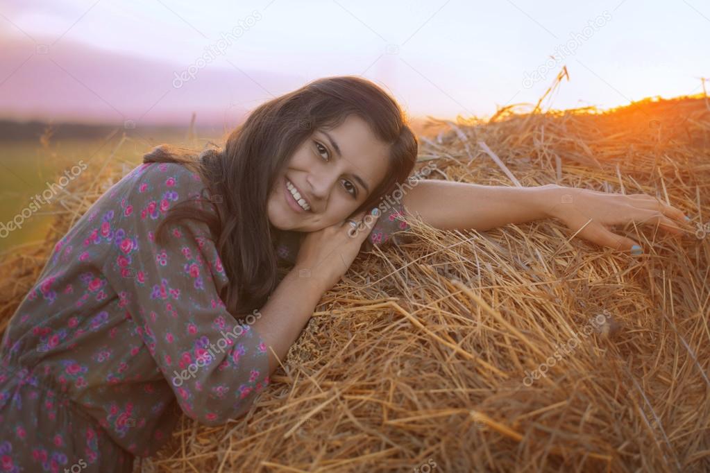 A beautiful girl was leaning against the haystack in the field