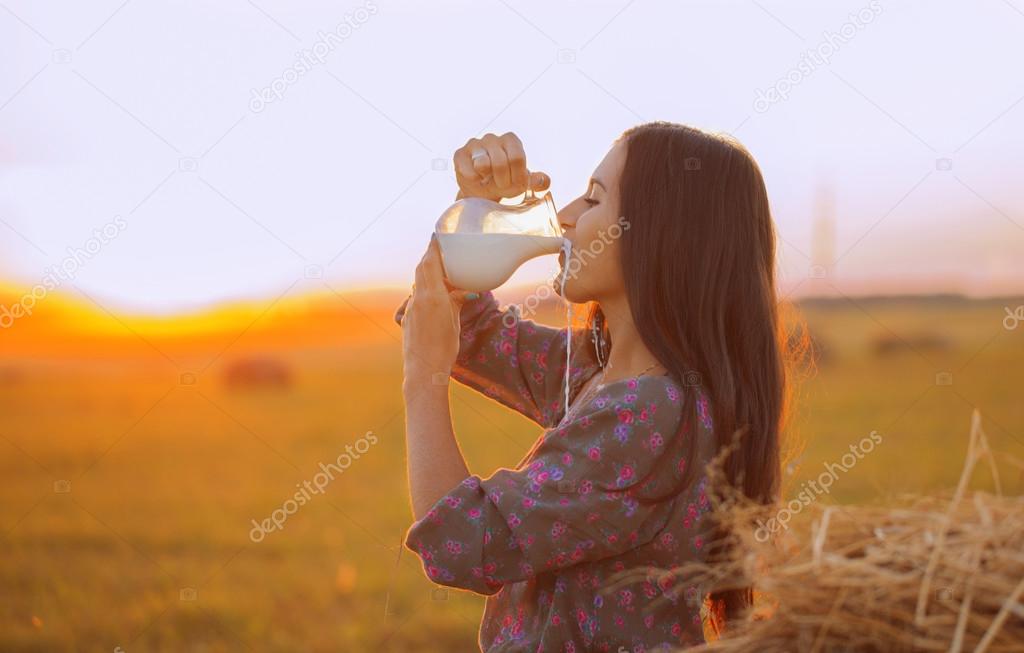 Beautiful brunette drinks milk in field at sunset