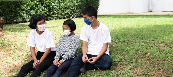 Trójka Dzieci Siedzi Parterze Zielonej Trawy Noszą Maski Aby Chronić — Zdjęcie stockowe