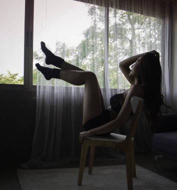 Küçük sutyen ve dar pantolon giyen, tahta koltukta oturan, portatif poz veren seksi bir kadının bulanık hareketi.